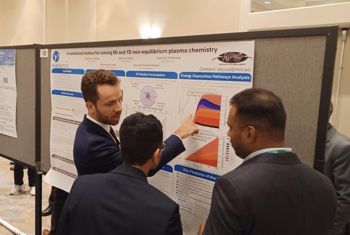 Member of the Aerospace Plasma Group showing his research poster to onlookers at a conference.